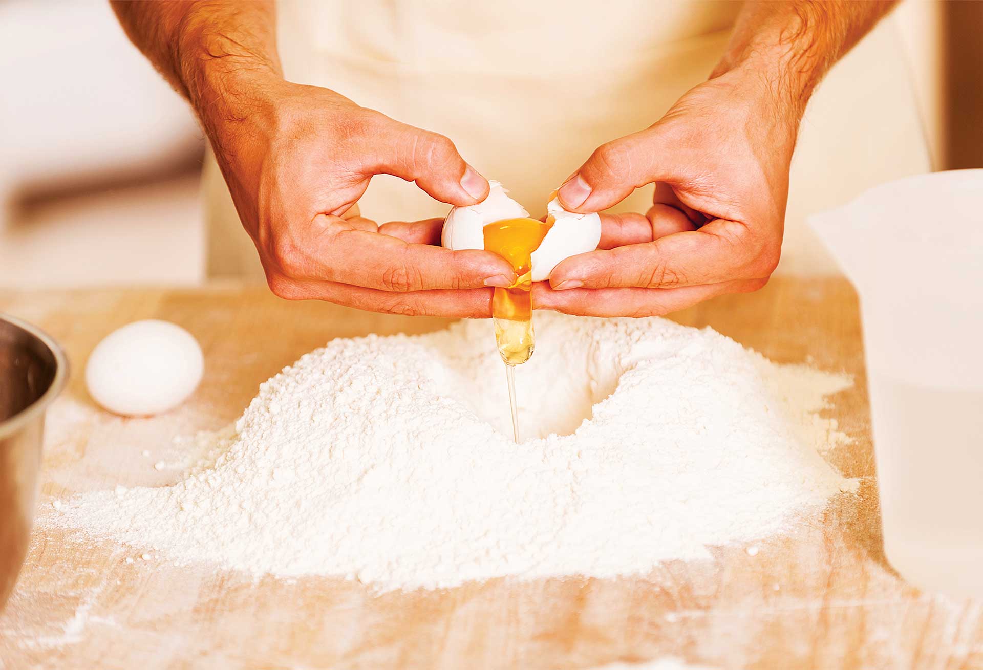 Photo of an egg being cracked over flour on a table top.